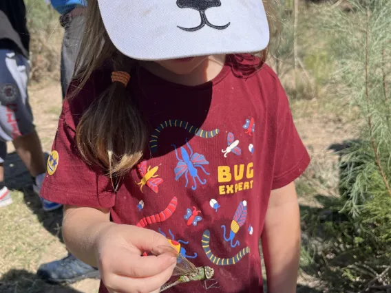 A child holding a dragonfly wearing a shirt that says Bug Expert