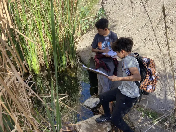 Students sitting next to water at Santa Cruz River