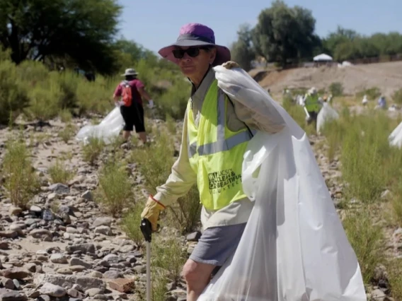 Woman holding a white trash bag in Santa Cruz River wearing yellow vest