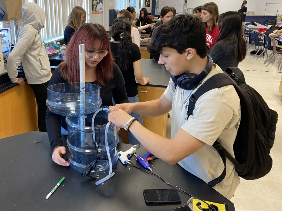 Two students building aquaponic system with large water bottles