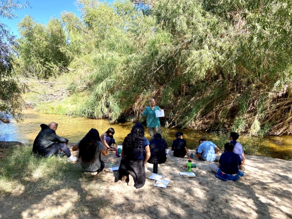 Teacher holding up paper in front of a group of students on the edge of the Santa Cruz River