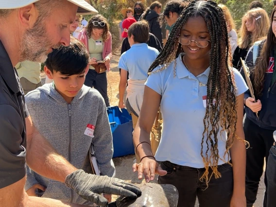 Two students touching a turtle being held by a professor at the Santa Cruz River