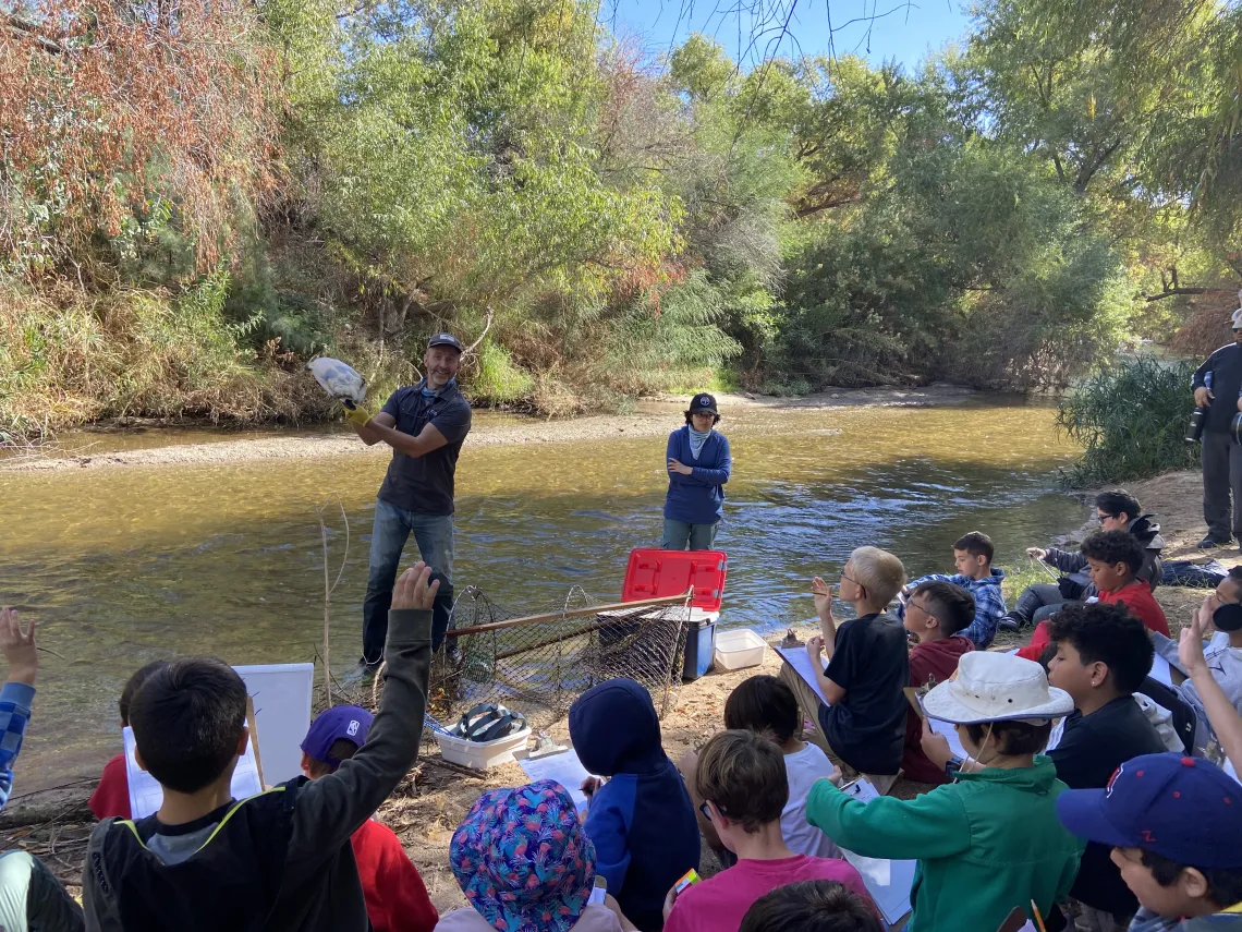 Person holding a turtle in front of a group of students on edge of river