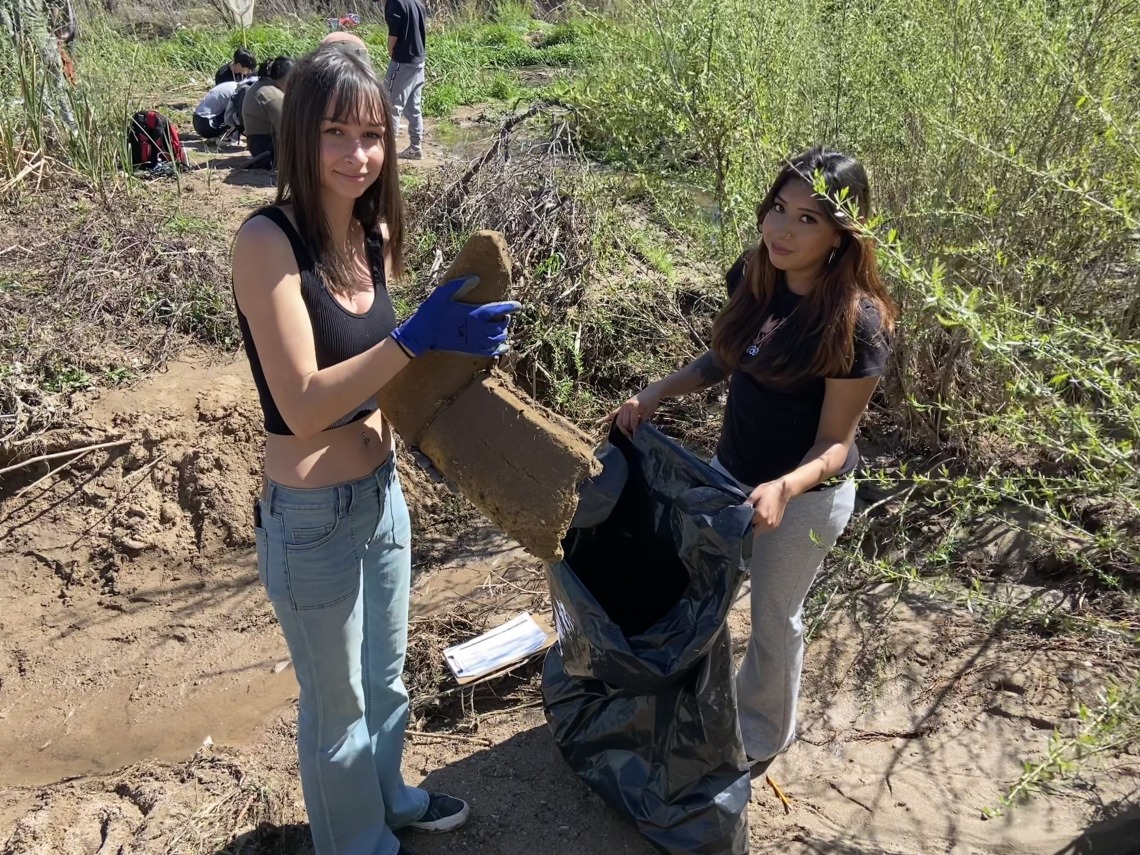 Two students adding trash to large bag