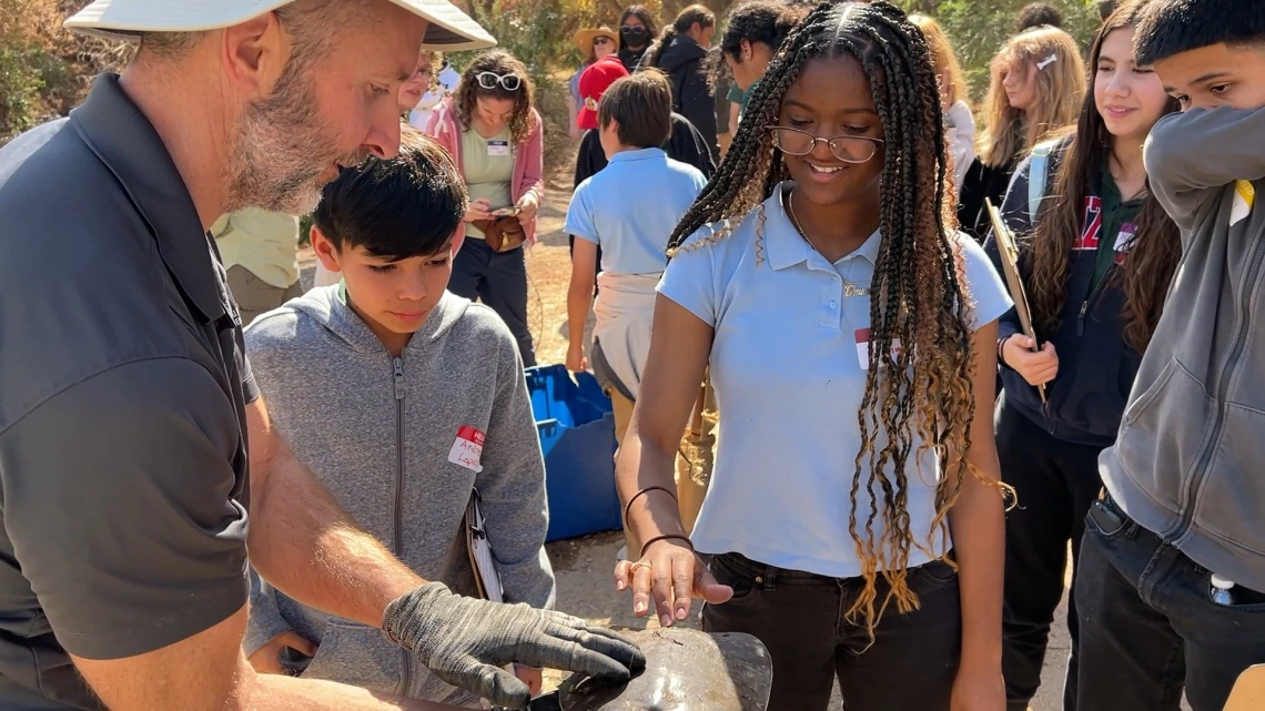 Two students touching a turtle being held by a professor at the Santa Cruz River